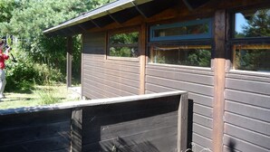 A wooden cabin with a sloped roof, multiple windows, and a view of surrounding trees. - Cozy cottage close to the beach (Liseleje)