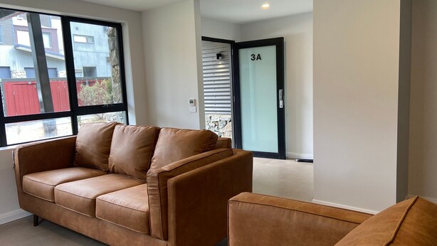 A modern living room with a brown leather sofa, a glass door with a number plate, and a view of the outside. - Blues Air 3A - Thredbo (Thredbo)