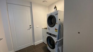 A laundry room with a stacked washer and dryer, a door, and a tiled floor. - Blues Air 3A - Thredbo (Thredbo)