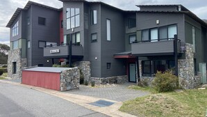 A modern multi-story building with a metal exterior, a red garage door, and a stone foundation. - Blues Air 3A - Thredbo (Thredbo)