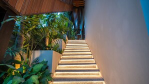 A staircase with illuminated steps, surrounded by lush greenery and a modern architectural design.