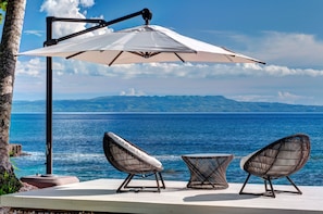 A deck with two wicker chairs and a small table, overlooking a body of water with distant land.
