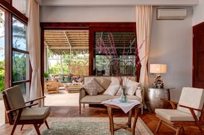 A spacious living area with a sofa, chairs, a coffee table, and a view of a garden through large windows.