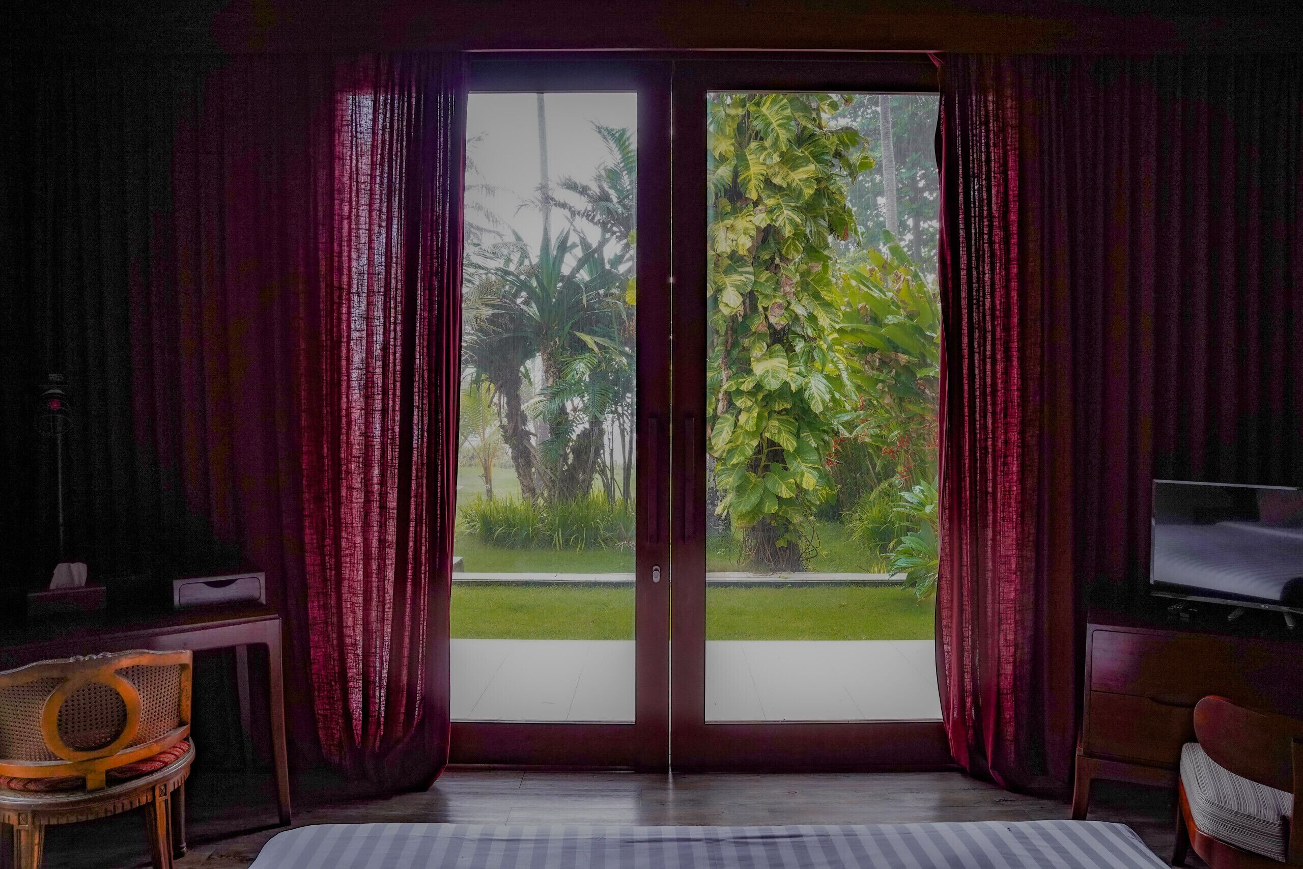 Une chambre dotée d’une porte-fenêtre coulissante donnant sur un jardin, d’un lit, d’une télévision et d’un fauteuil.