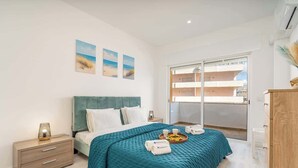 Un dormitorio moderno con cama, mesita de noche, cómoda y balcón con vistas.