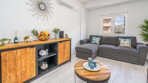 Una sala de estar moderna con un sofá seccional gris, un mueble de madera con estantes, una mesa redonda de centro y un reloj de pared decorativo.