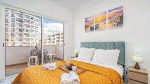 Habitación de hotel con una cama grande, un balcón con vista a otros edificios y obras de arte en la pared.