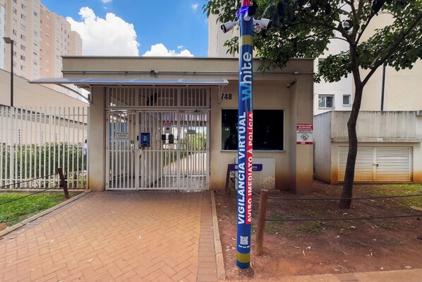A gated entrance with a metal gate, a surveillance camera on a pole, and a sign indicating a virtual vigil.