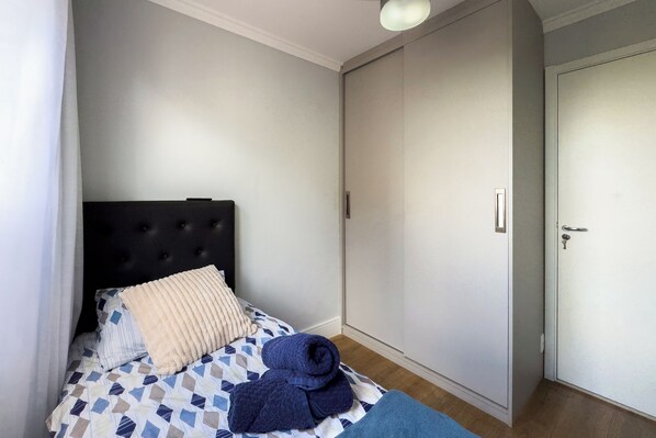A bedroom with a bed, a black headboard, a white door, and a wardrobe.