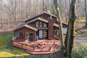 Une cabane en bois dotée d’une terrasse, de grandes fenêtres et d’une cheminée.