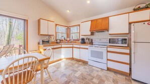 Eine moderne Küche mit weißen Schränken, einer Mikrowelle, einem Backofen und einem Kühlschrank. Ein Esstisch mit Stühlen und ein Fenster sorgen für natürliches Licht.