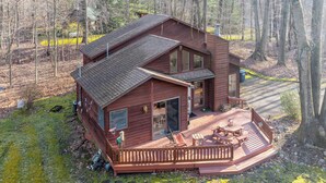 Eine zweistöckige Holzhütte mit einer Terrasse, umgeben von Bäumen.