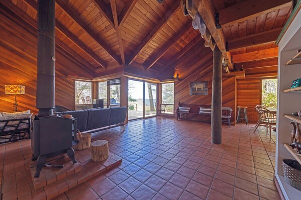 A spacious room with a large fireplace, wooden ceiling, and a view of the outdoors.
