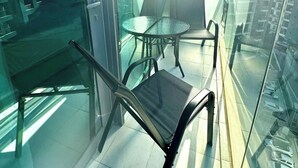 A modern balcony with a glass table and chairs, offering a view of a high-rise building.