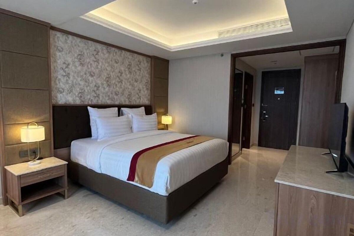 Una habitación de hotel con una cama grande, lámparas de noche, un televisor de pantalla plana y una mesita de noche de madera.