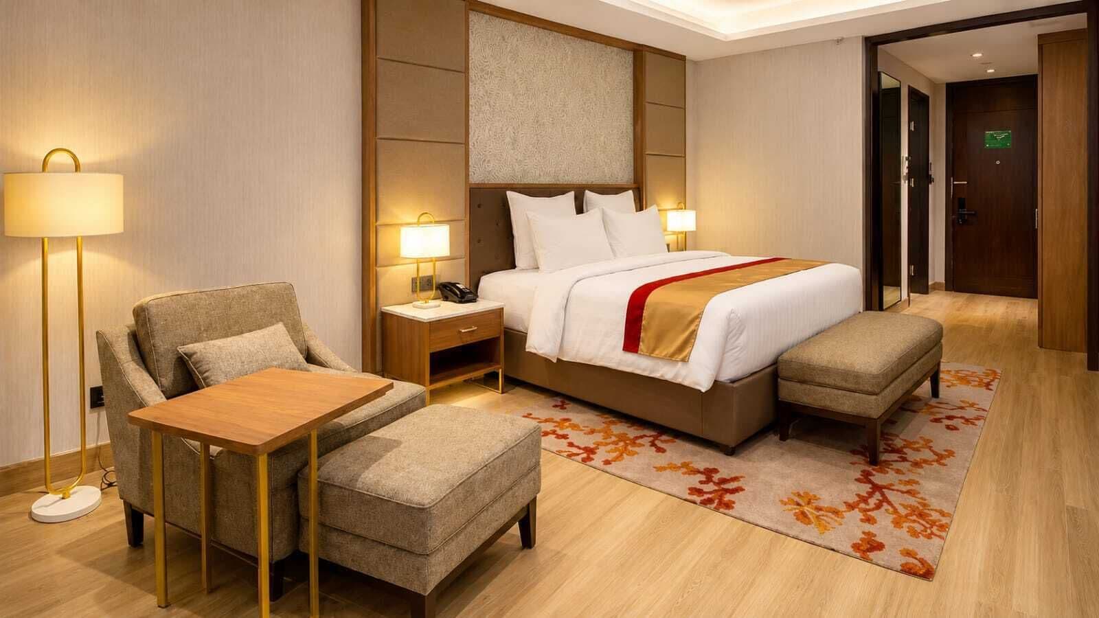 A hotel room with a bed, bedside tables, a desk, a chair, and a floor lamp.