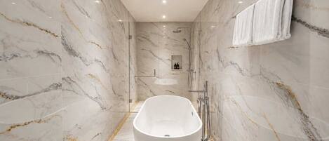 A modern bathroom with a freestanding bathtub, marble walls, and a glass-enclosed shower area.