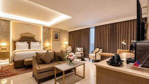 A hotel room with a bed, a sofa, a coffee table, a desk with a coffee machine, and a TV. - Grand Travello Hotel Bekasi (Bekasi)