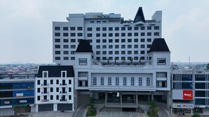 A large, modern building with a prominent 'Grand TRAVELLO' sign. It features multiple floors, a central entrance with a staircase, and a parking area in front. - Grand Travello Hotel Bekasi (Bekasi)