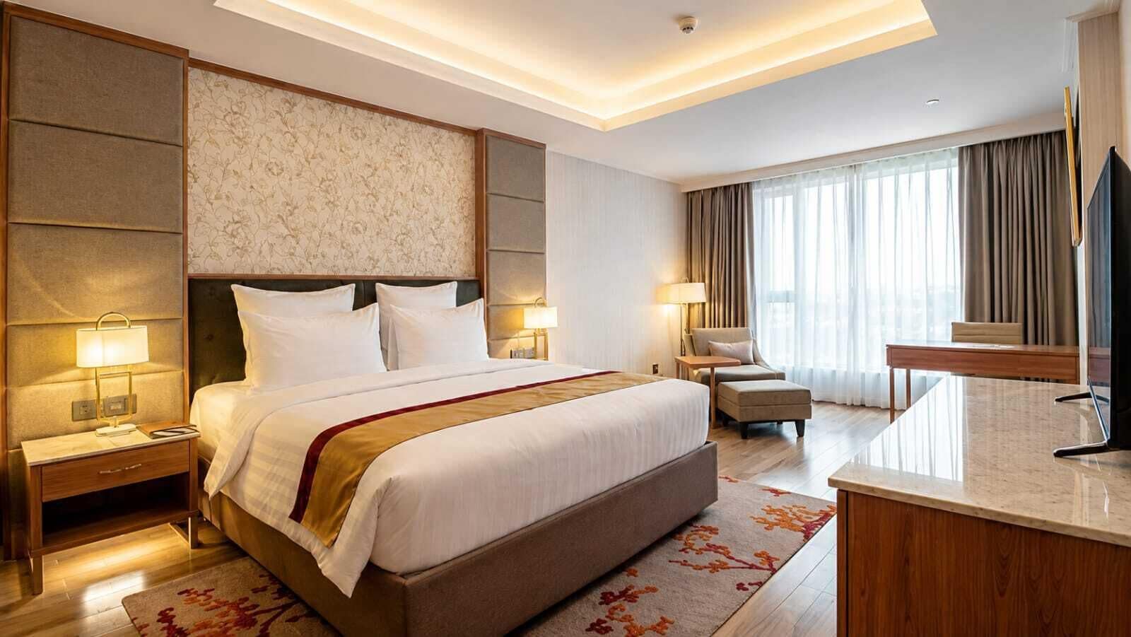 A hotel room with a large bed, bedside tables, a desk, a chair, and a TV.