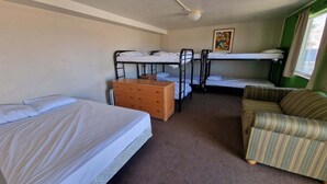 A room with bunk beds, a wooden dresser, a striped armchair, and a painting on the wall. - Family Suite - Economy (Garden City)