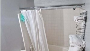 A bathroom with a toilet, a shower with a curtain, a bathtub, and a tiled floor. - Family Suite - Economy (Garden City)