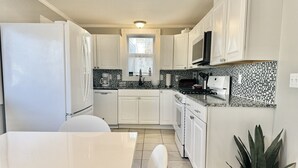 A compact kitchen with white cabinets, a tiled backsplash, and a central island with seating. - House Acadia at Gallagher`s Travels (Bar Harbor)
