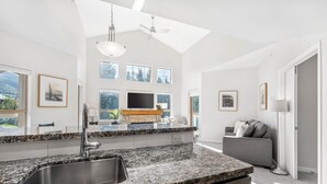 A modern kitchen with granite countertops, a stainless steel sink, and a built-in oven. There is a large window with a view of trees and mountains. - 2BR + Loft + Sofabed | Tyndall Stone Lodge | Epic Village Location | Mountain Views | Pool & Hot Tub (Whistler)