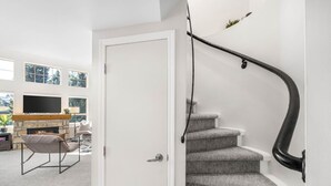 A modern interior with a staircase, a fireplace, and a living area with a TV and seating. - 2BR + Loft + Sofabed | Tyndall Stone Lodge | Epic Village Location | Mountain Views | Pool & Hot Tub (Whistler)