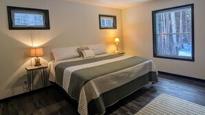 A bedroom with a bed, two bedside lamps, a ceiling fan, and two framed pictures on the walls. - Charming quiet 2-bedroom house set in a cedar forest in welcoming Fish Creek (Fish Creek)