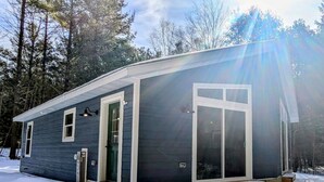 A small, single-story cabin with a dark exterior, white trim, and a front door. - Charming quiet 2-bedroom house set in a cedar forest in welcoming Fish Creek (Fish Creek)