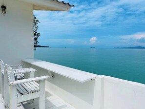 Ein Balkon mit weißer Brüstung, der auf ein ruhiges Meer und entferntes Land blickt.