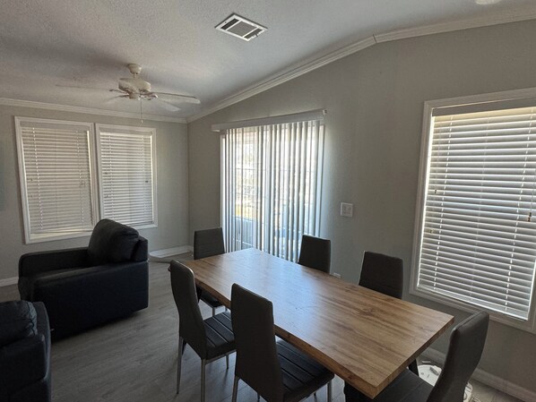 Un comedor con mesa y sillas de madera, un sofá oscuro y un ventilador de techo.