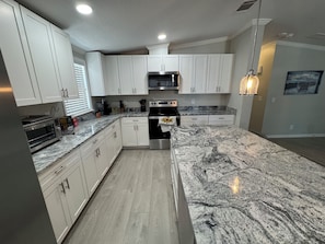 Una cocina moderna con armarios blancos, encimera de granito, electrodomésticos de acero inoxidable y una lámpara colgante.