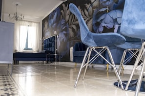 A modern living room with a large floral mural, a sofa, a chair, and a chandelier. - "Antiquarian's Loft" (Tempio Pausania)