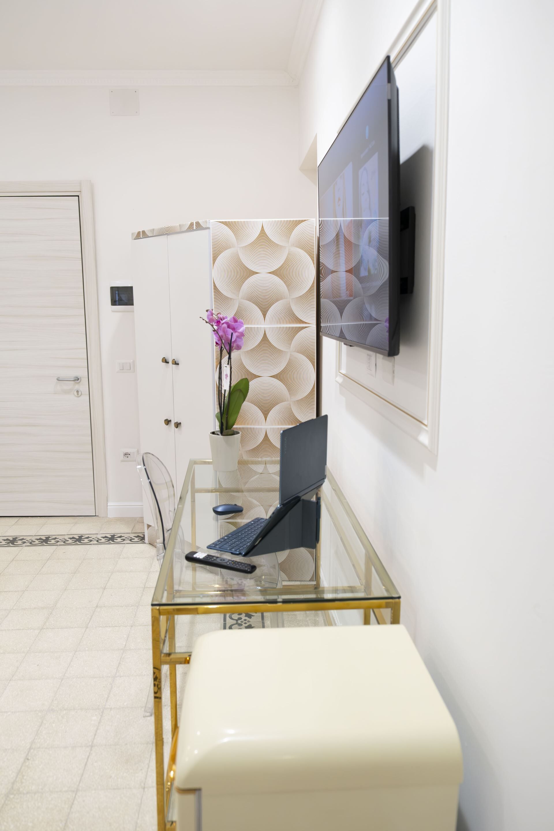 Een moderne kantoorruimte met een glazen bureau, een laptop, een potorkidee en een televisie aan de muur.