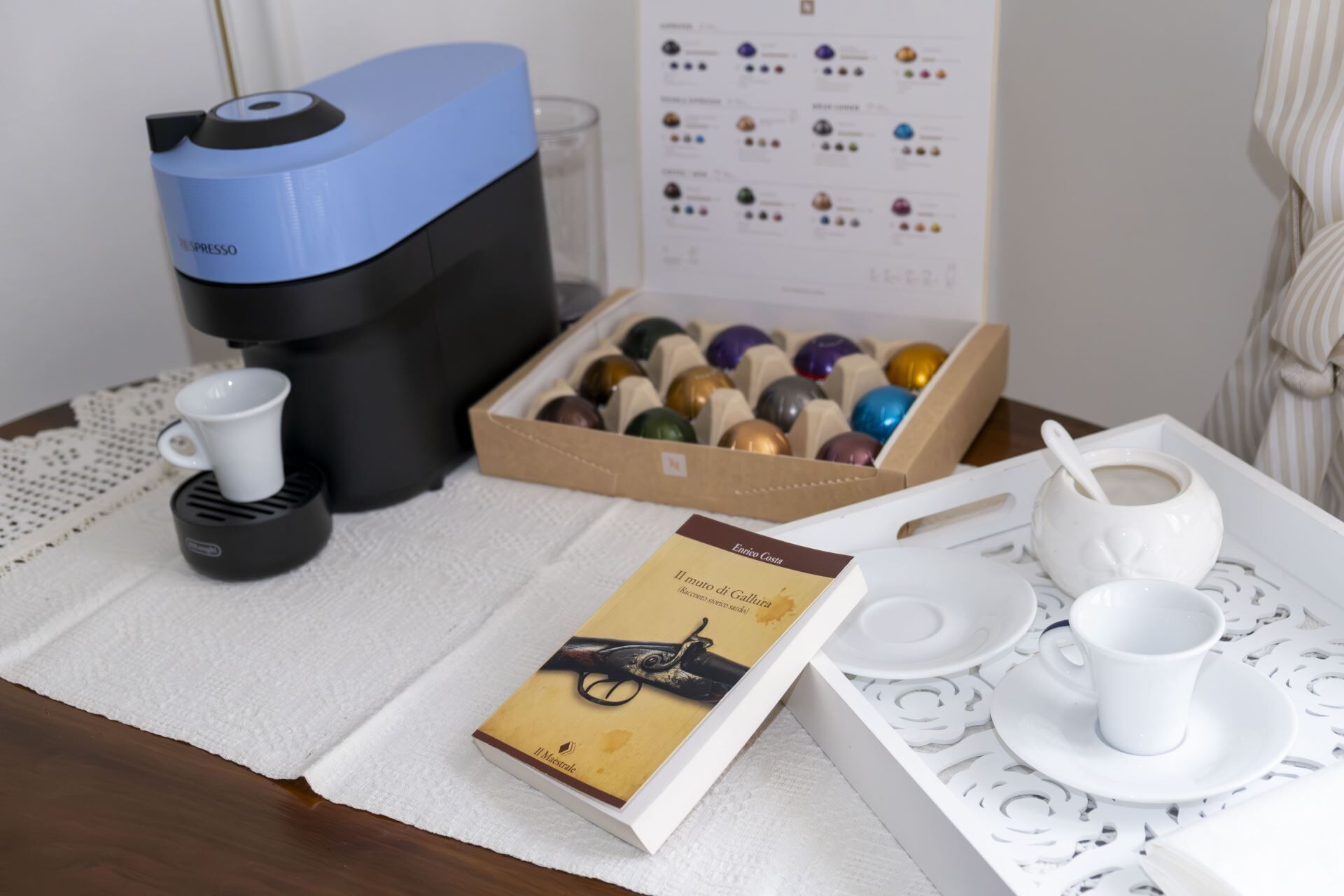 A coffee machine, a box of chocolates, a book, and a tray with cups and saucers on a table.