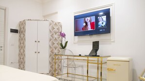 A hotel room with a bed, a desk with a laptop, a television mounted on the wall, and a minibar.