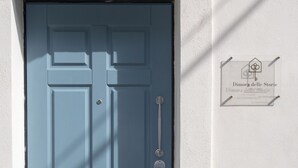 A blue door with a handle and a keyhole, a small sign with the number 6, and a potted plant to the right.