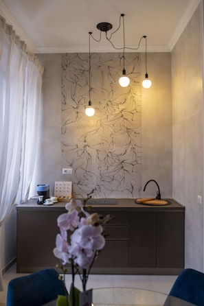 Uma cozinha moderna com painel de parede de mármore, luminárias pendentes, pia e cafeteira.