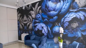 Un salon moderne avec un canapé bleu, une table basse en verre et une fresque murale à motifs floraux.