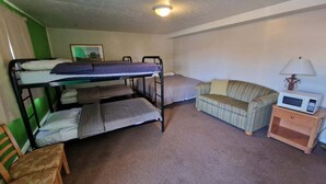 A bunk bed with a lower bunk, a single bed, a striped sofa, a wooden nightstand with a microwave, and a lamp.