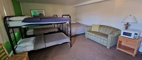 A bunk bed with a lower bunk, a single bed, a striped sofa, a wooden nightstand with a microwave, and a lamp.