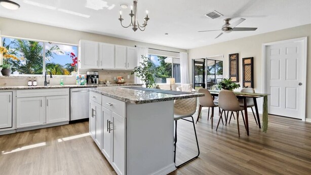 A modern kitchen with white cabinets, a granite countertop island, and a dining area with a table and chairs. - 4BR, 2BA with Heated Pool, BBQ, Fire pit in Port St. Lucie (Port St. Lucie)