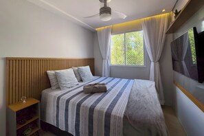 Una cama bien tendida con ropa de cama a rayas, un cabecero de madera, una mesita de noche con una copa y una ventana con cortinas.