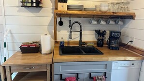 Una cocina compacta con encimera de madera, un fregadero, una cafetera y un lavavajillas.