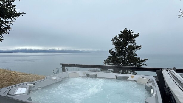 A hot tub with a view of a lake and mountains. - Dall Cabin - Cozy retreat with bay views, a shared hot tub, and fire pit! (Homer)