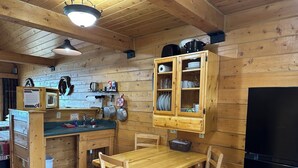 Eine Holzhütte mit einer Küche, einem Holztisch und Stühlen, einem schwarzen Kühlschrank und einem Schrank mit Geschirr.