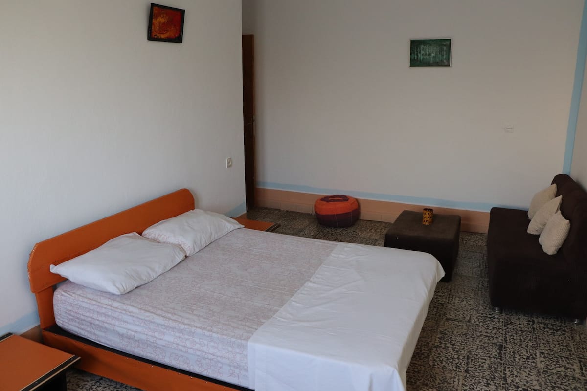 Un dormitorio con cama, mesita de noche, sofá y dos obras de arte colgadas en la pared.