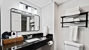 Un bany amb taulell negre, un lavabo, un vàter, un mirall i prestatges amb tovalloles.
